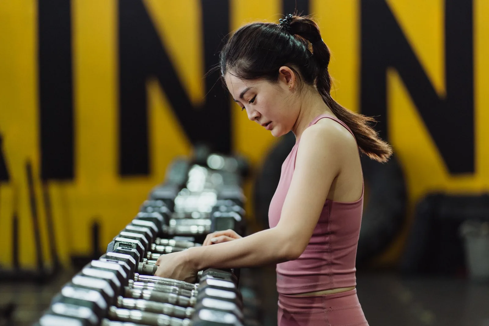 Mujer eligiendo mancuernas en el gimnasio para mantener la constancia
